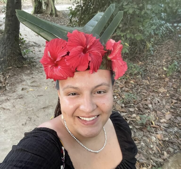 A woman smiling while wearing a traditional floral headpiece made from hibiscus flowers and green leaves in Zanzibar's natural setting