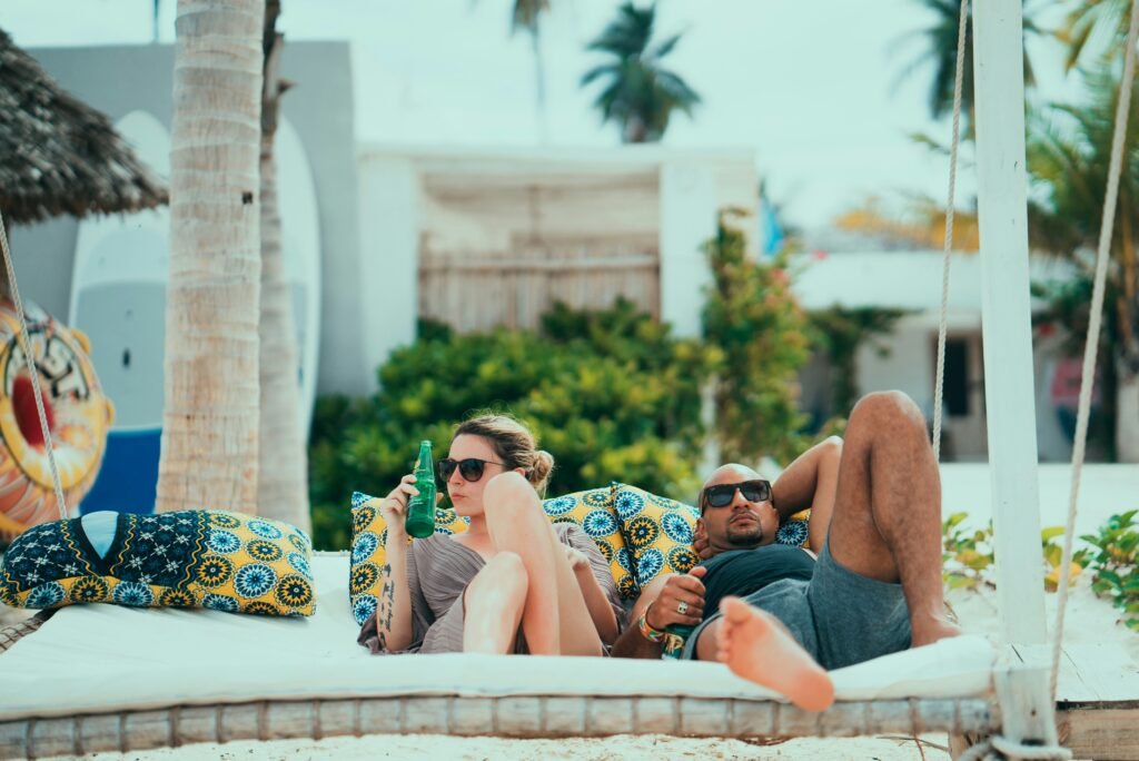 A couple lounging on a swing bed with vibrant cushions under palm trees, enjoying a relaxing moment near the beach in Zanzibar.