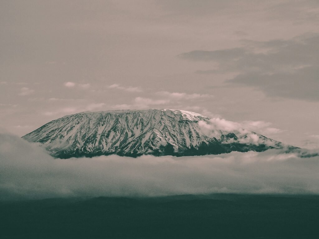 A dramatic view of Mount Kilimanjaro, its snow-capped peak emerging above the clouds, captured in a moody, monochrome setting.